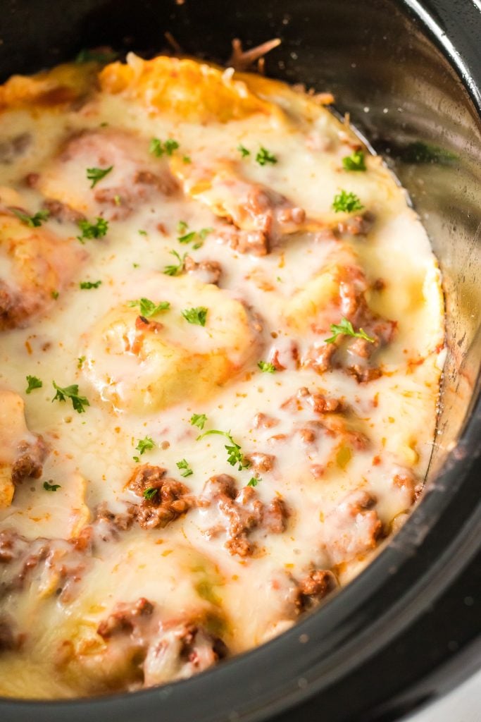 closeup of cheesy ravioli garnished with parsley in a crockpot.