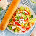 overhead shot of a vegetable chopped salad with a breadstick in a bowl.