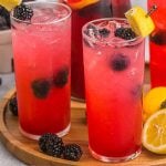 try of glasses filled with blackberry lemonade surrounded by lemons.