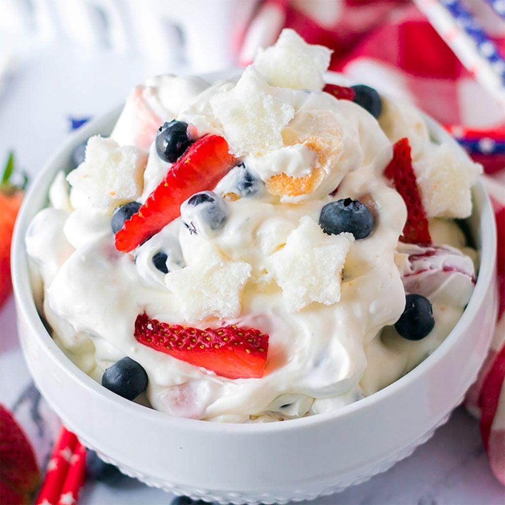 closeup of berry cheesecake fluff salad in a white bowl topped with berries.