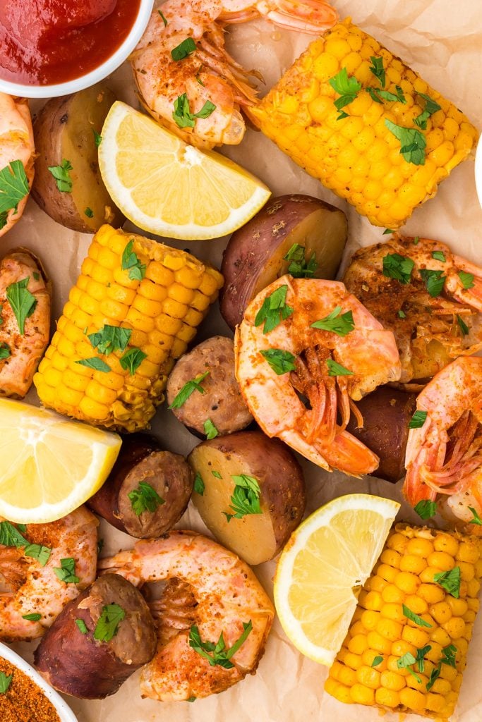 closeup shot of shrimp, corn, potatoes, and lemons laid out on parchment paper.