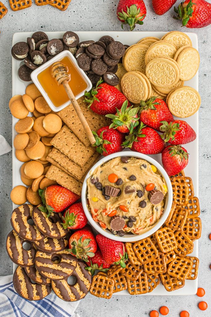 dessert board with sweet dip, strawberries, pretzels, and cookies.