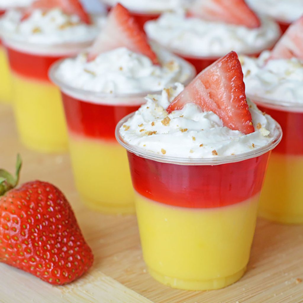 layered strawberry shortcake jello shot topped with whipped cream, nilla wafer crumbs, and strawberry slice. 