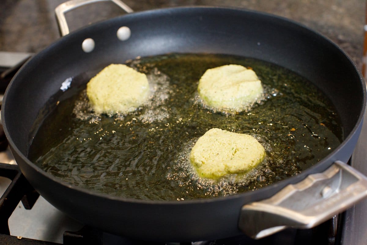 Falafel patties in a skillet, frying in oil.