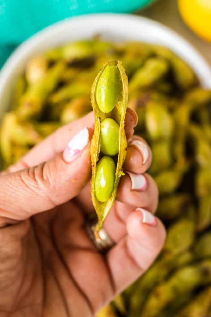 hand holding edamame showing the soybeans inside.