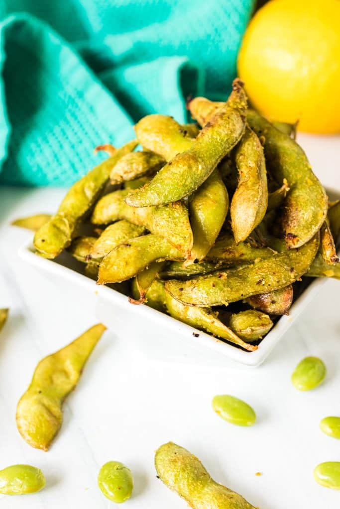 white bowl filled with air fried edamame and a teal linen.