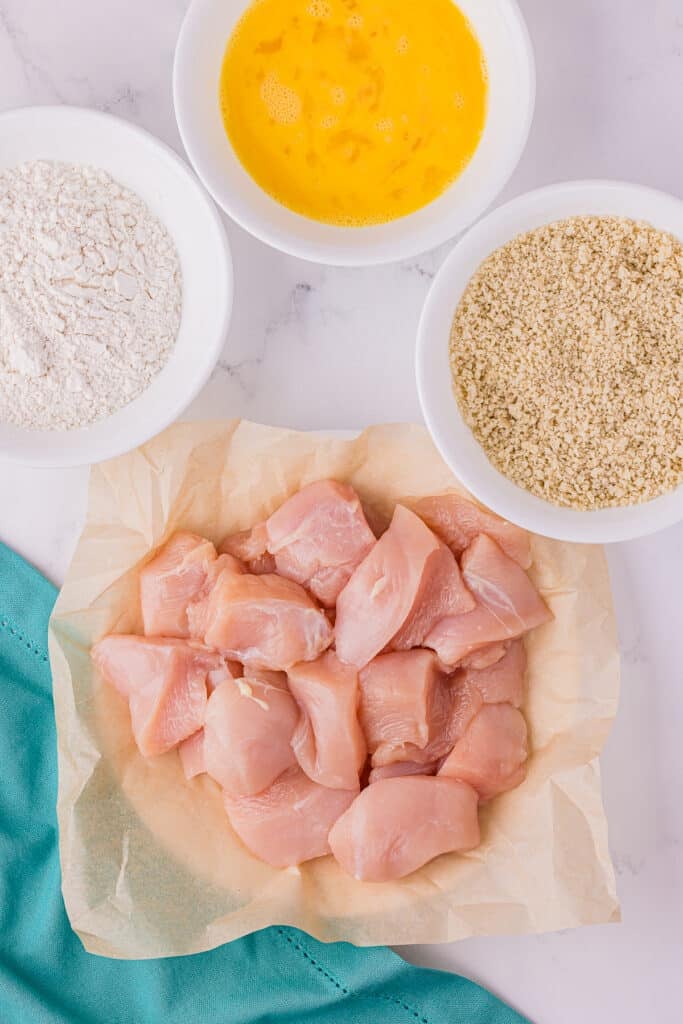 raw chicken breast cut into pieces next to a dredging station.