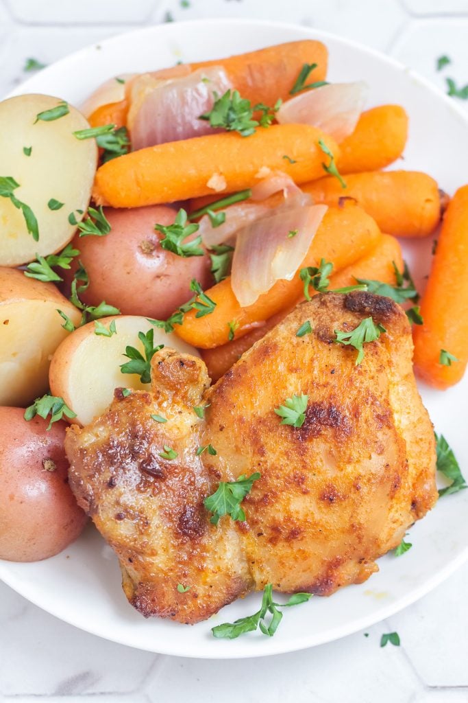 white plate with a seared chicken thigh next to red potatoes & carrots.