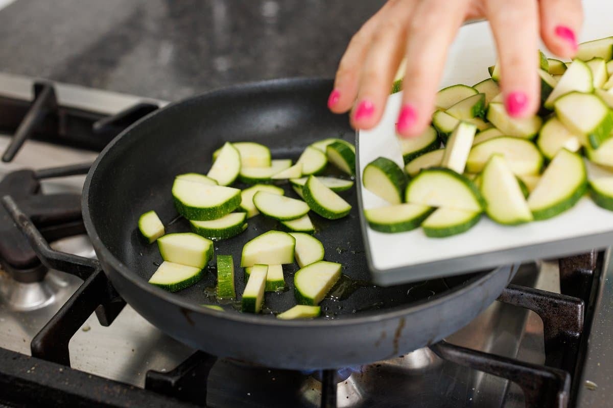 Adding zucchini slices to a sauté pan.