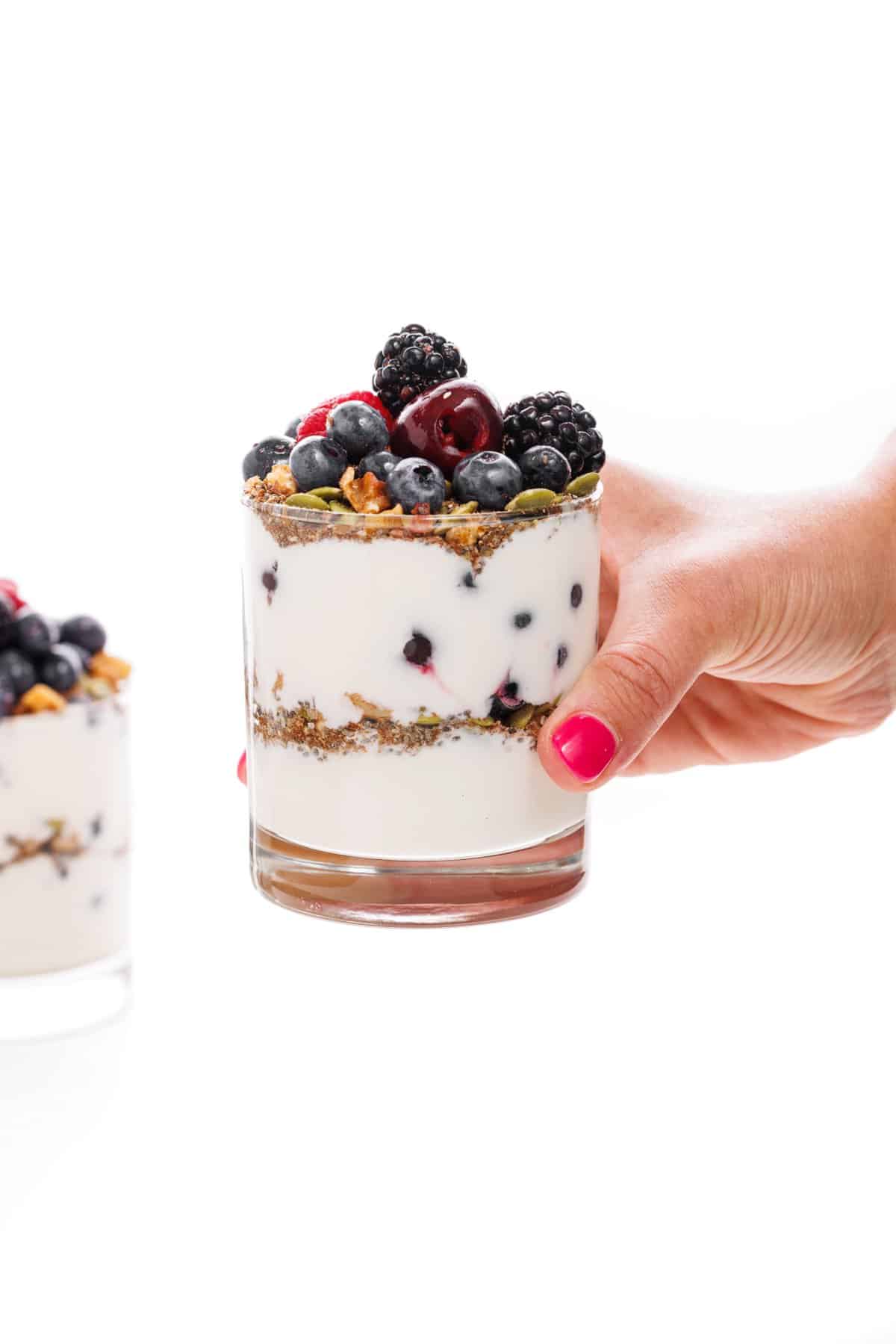 Holding a make-ahead fruit and yogurt protein parfait in a glass cup.