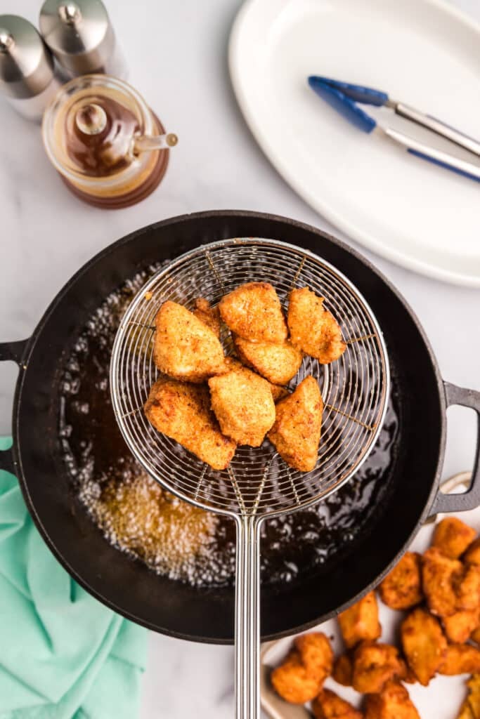 Golden fried chicken nuggets being lifted from oil with a wire skimmer.