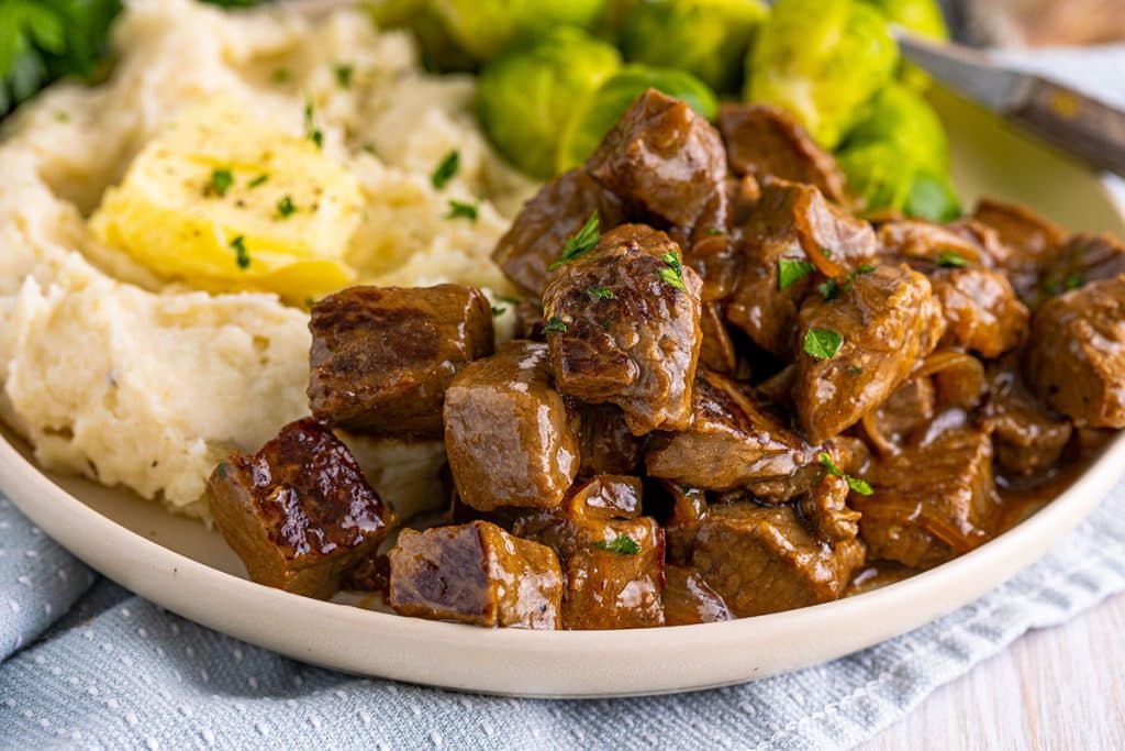 closeup of steak bites in gravy on a dinner plate.