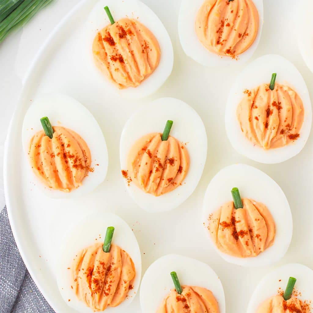 pumpkin shaped deviled eggs on a white platter.
