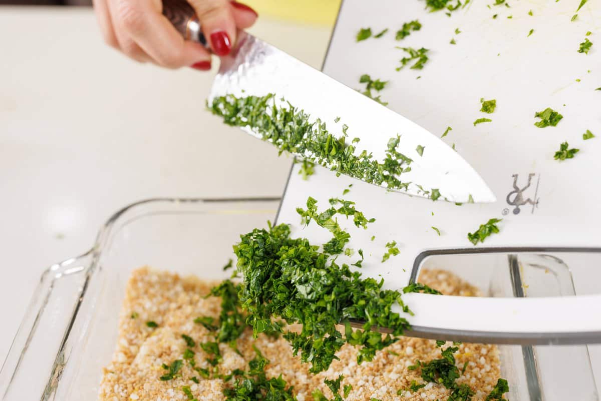 Adding freshly chopped parsley to pan of bread crumbs.