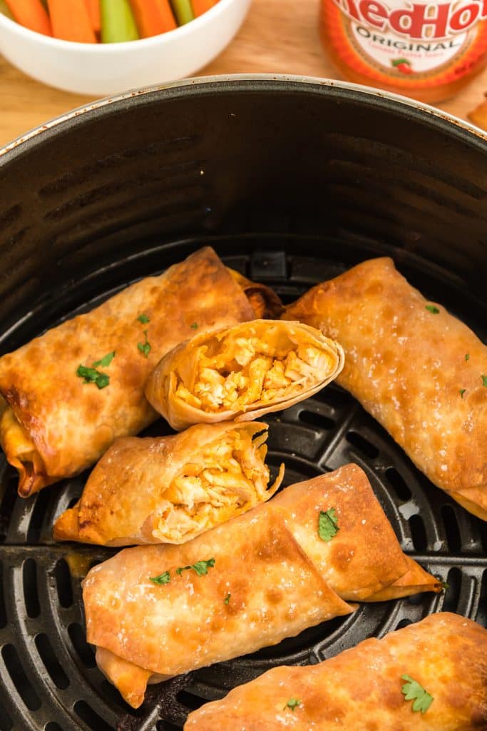 buffalo chicken egg rolls sitting in an air fryer basket.