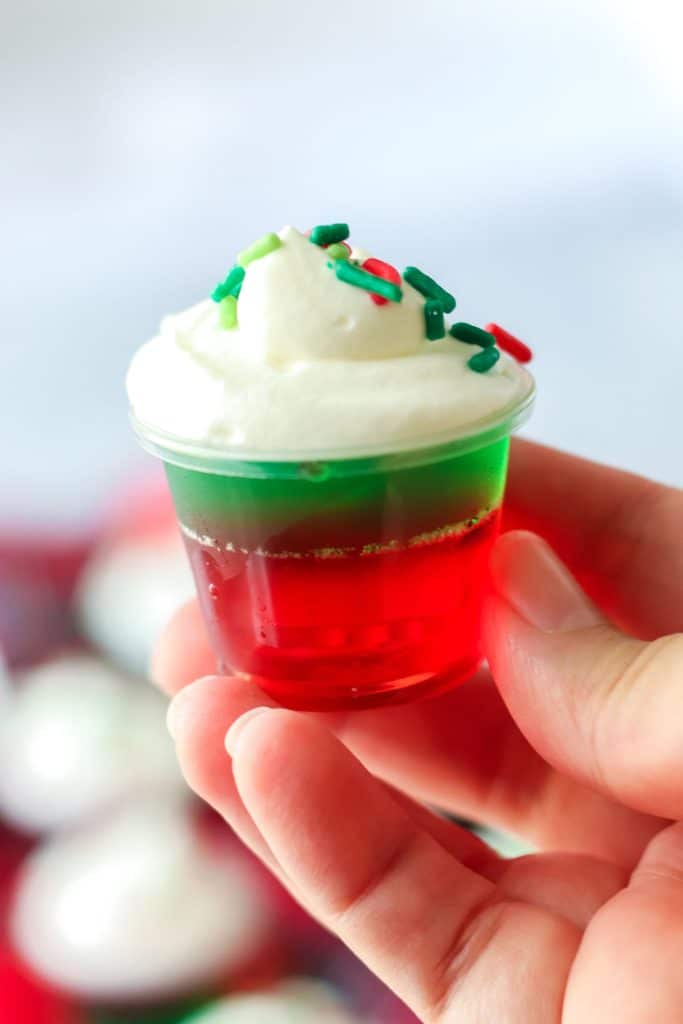 hand holding a christmas jello shot topped with whipped cream.