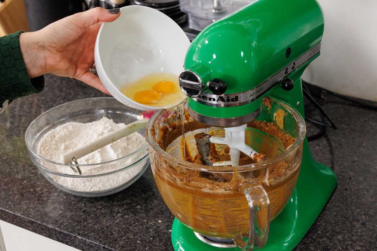 Adding two eggs to the bowl of a stand mixer.
