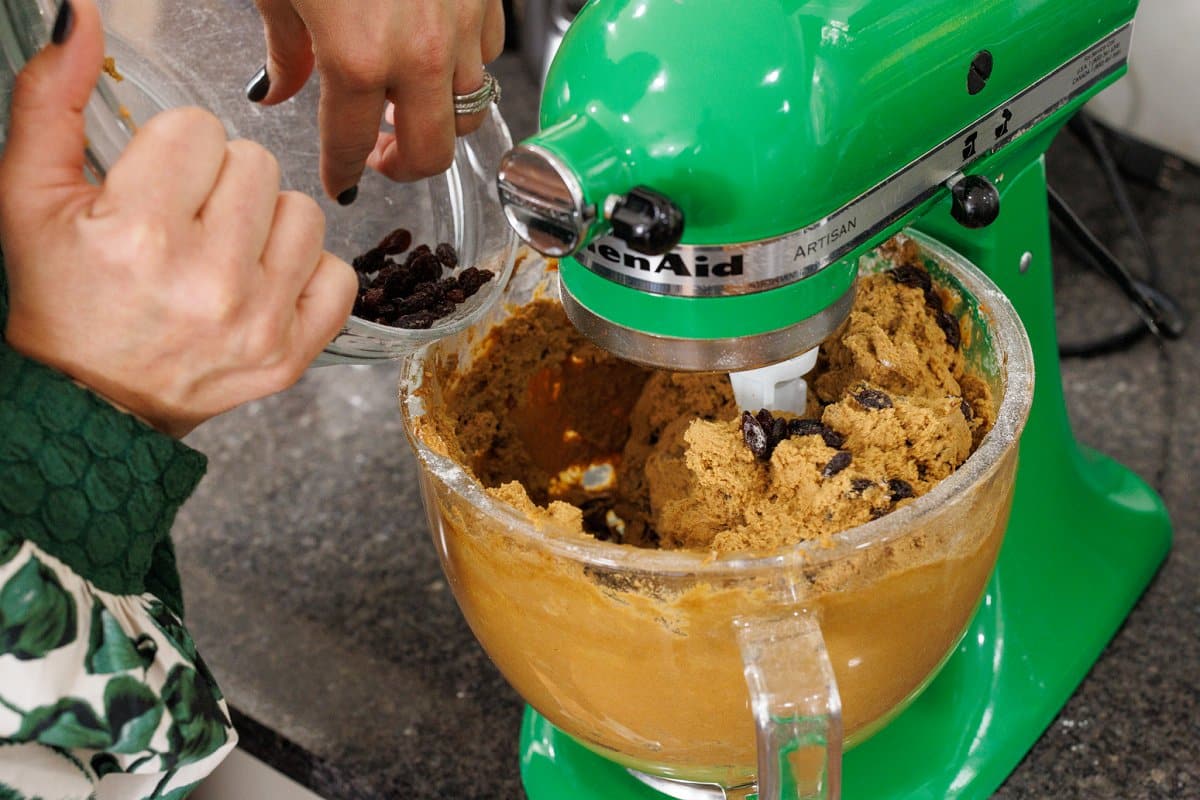 Slowly adding raisins to cookie dough in stand mixer bowl.