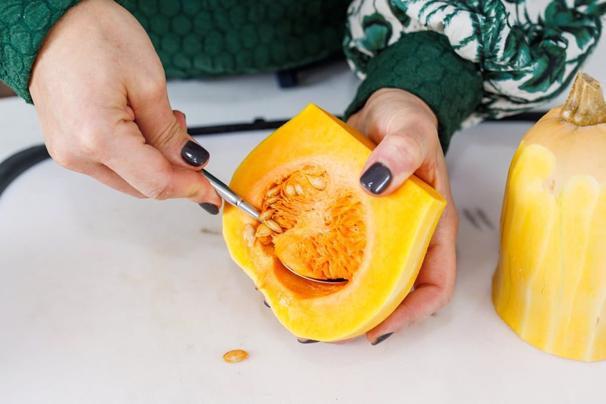 Scooping seeds out of butternut squash with a spoon.