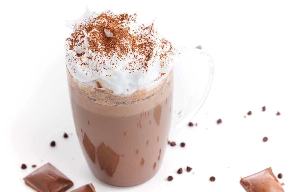 Dark chocolate hot cocoa topped with whipped cream and cinnamon, surrounded by scattered chocolate.