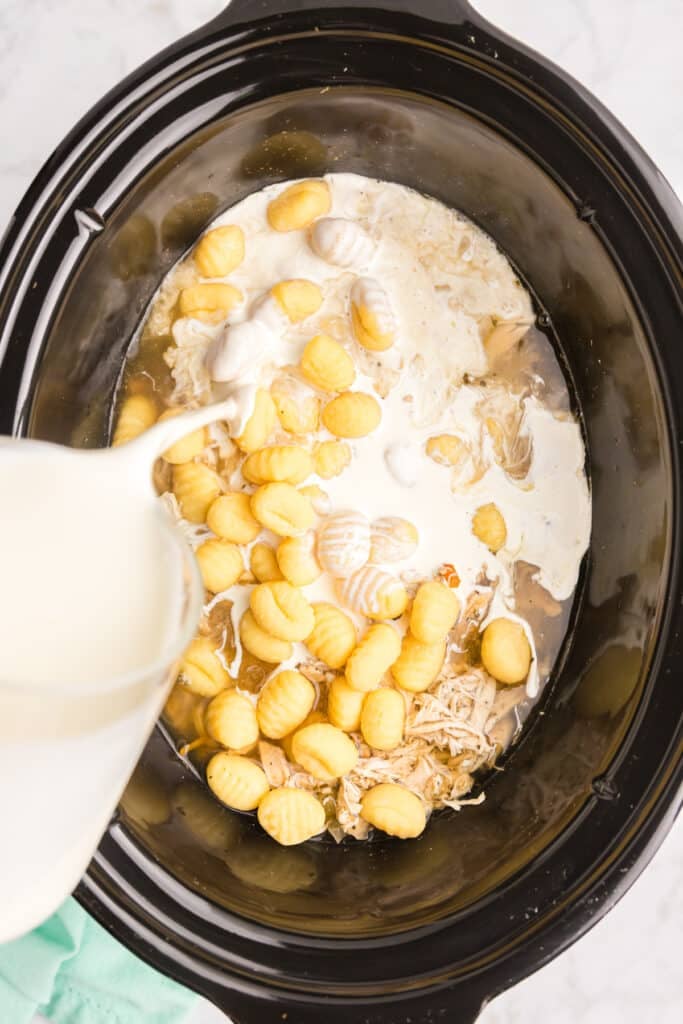 heavy cream pouring into a crockpot with gnocchi.