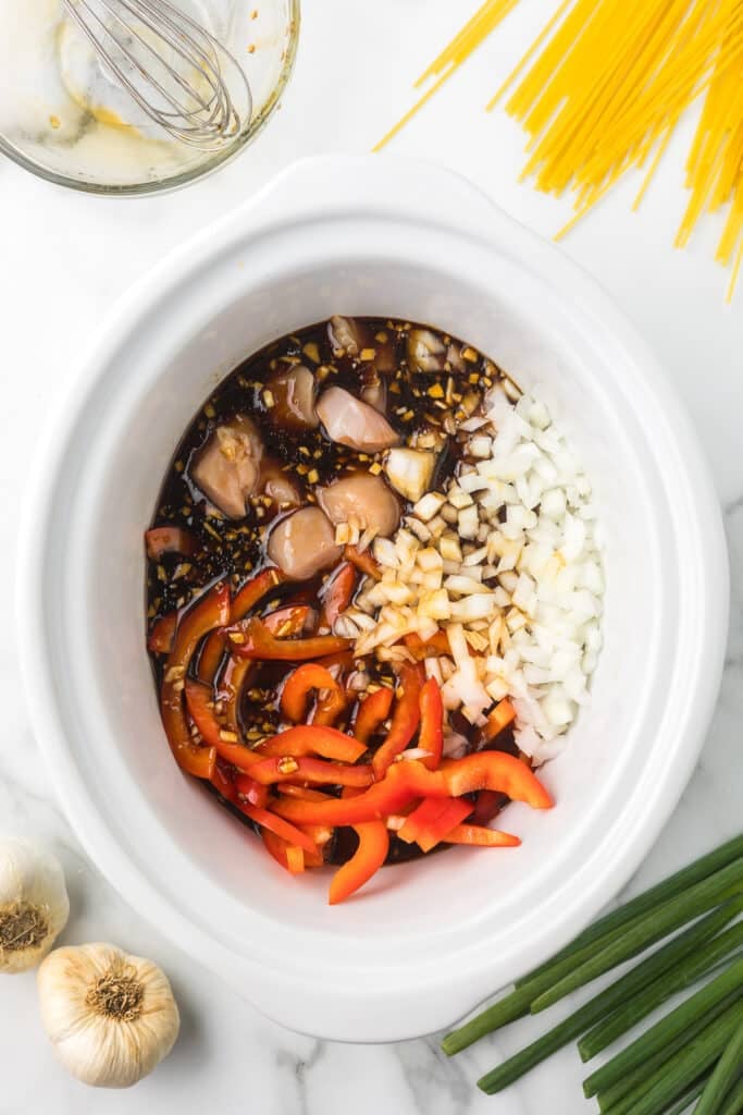 overhead sauce of peppers, onions, chicken, and sauce in a slow cooker.