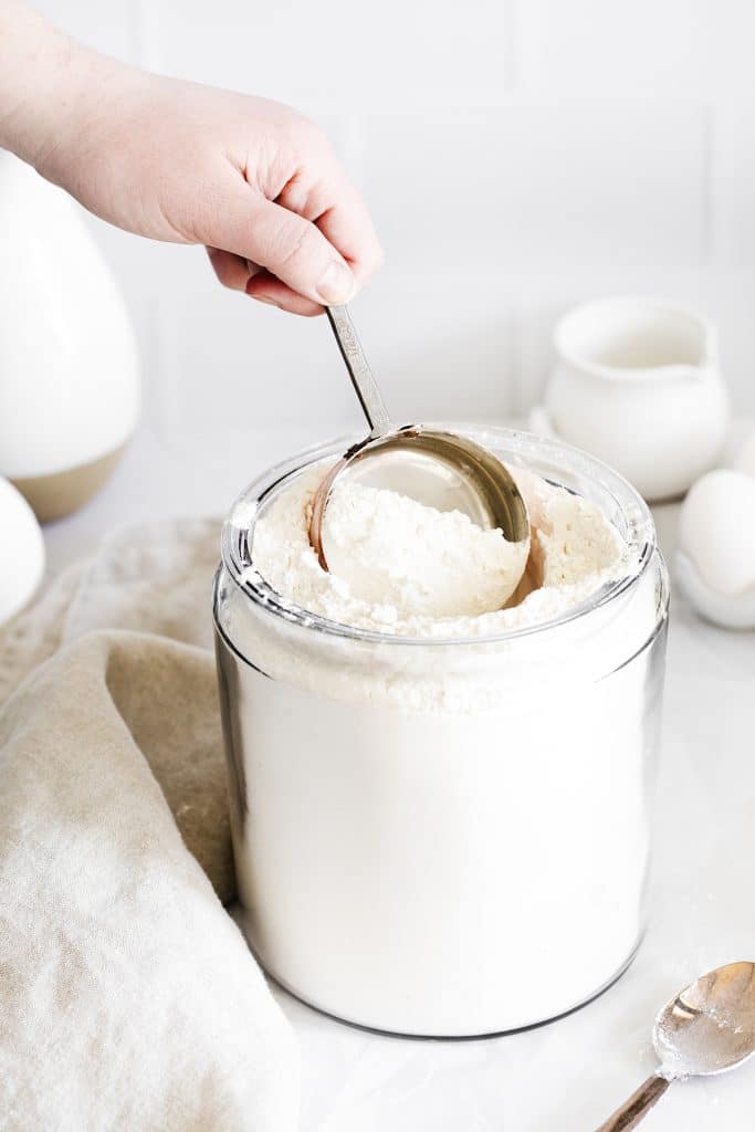 hand scooping flour from a glass jar.