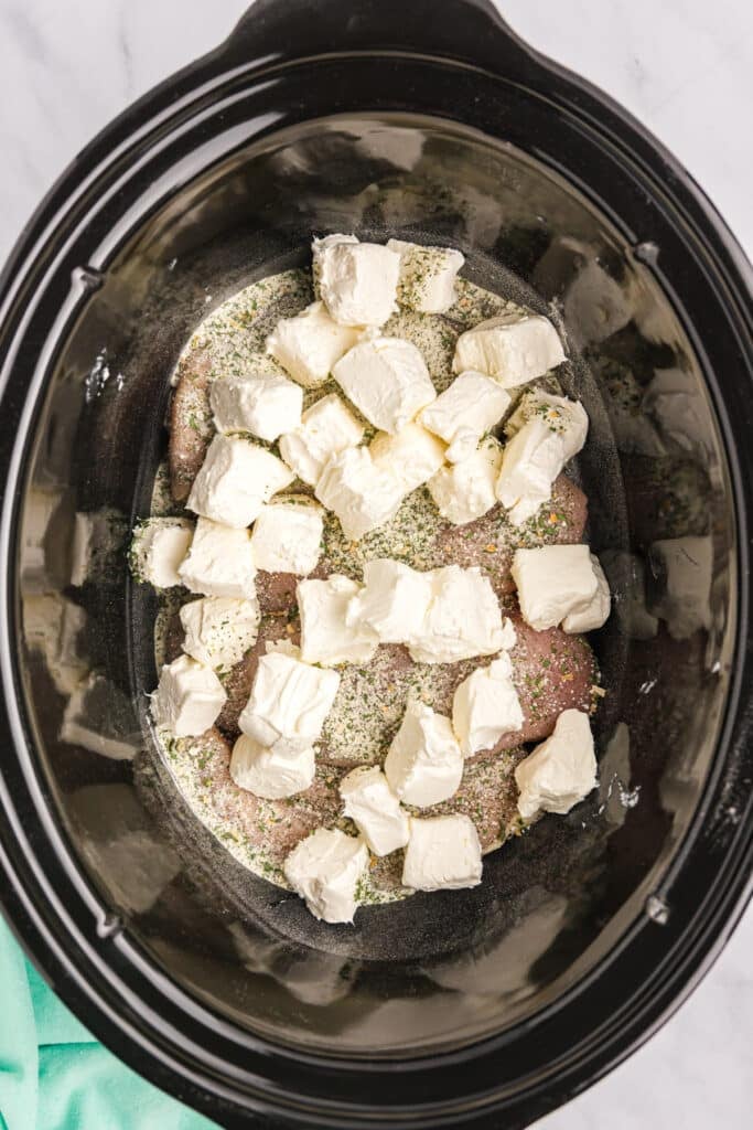 cubed cream cheese on chicken in a slow cooker.