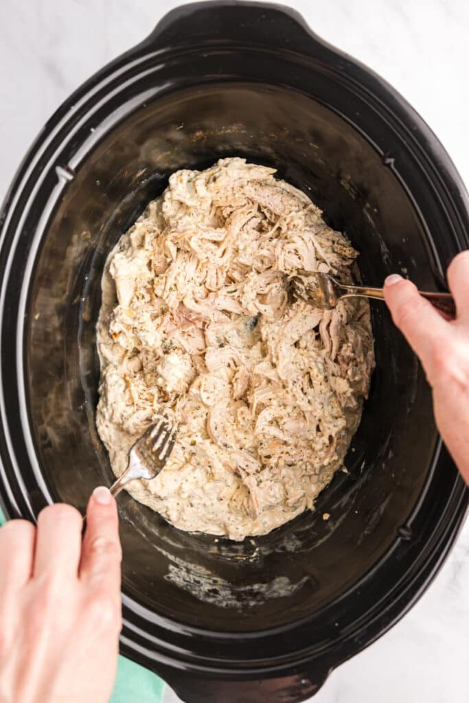 two forks shredding chicken in a crockpot.