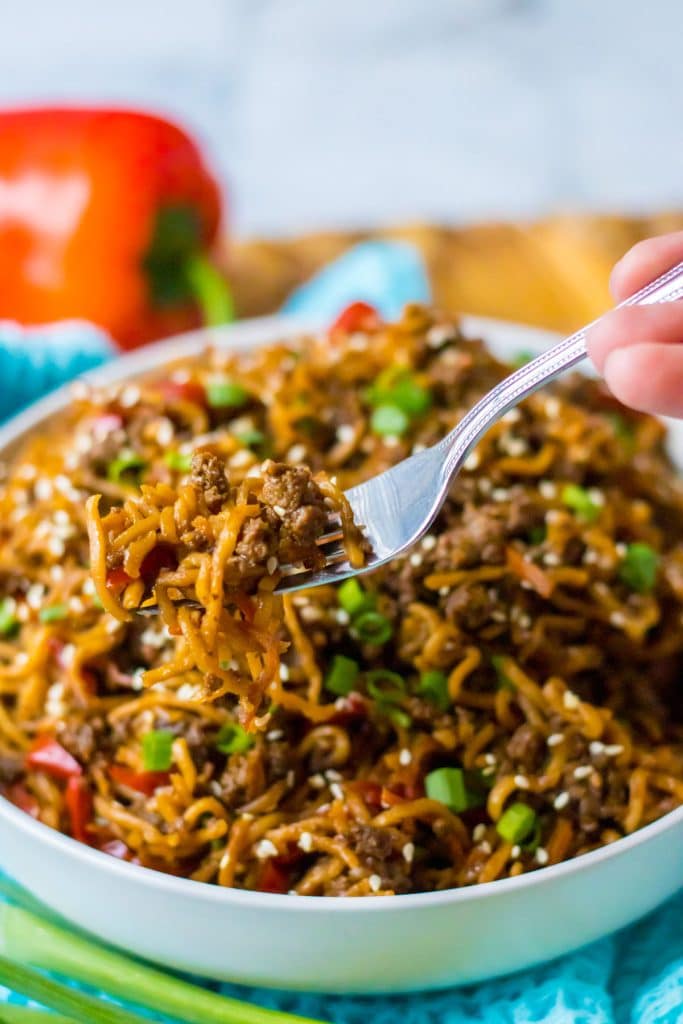 fork taking a bite of beefy ramen noodles from a white bowl.