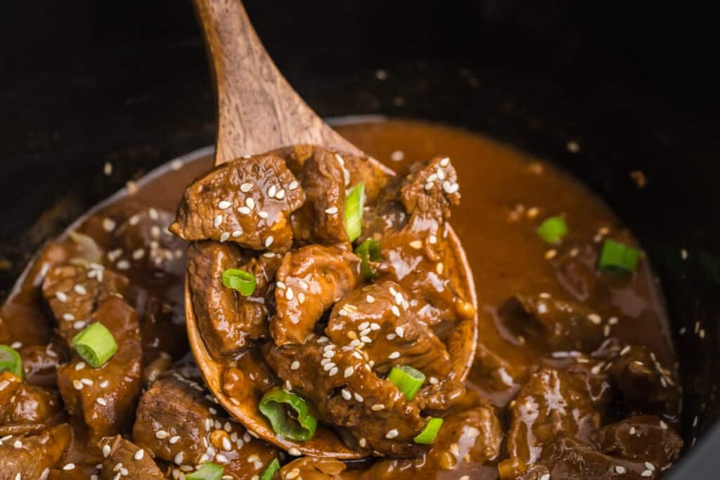 spoon scooping honey garlic steak bites from a crockpot.