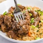 fork grabbing a bite of honey garlic steak bites on a plate with fried rice.