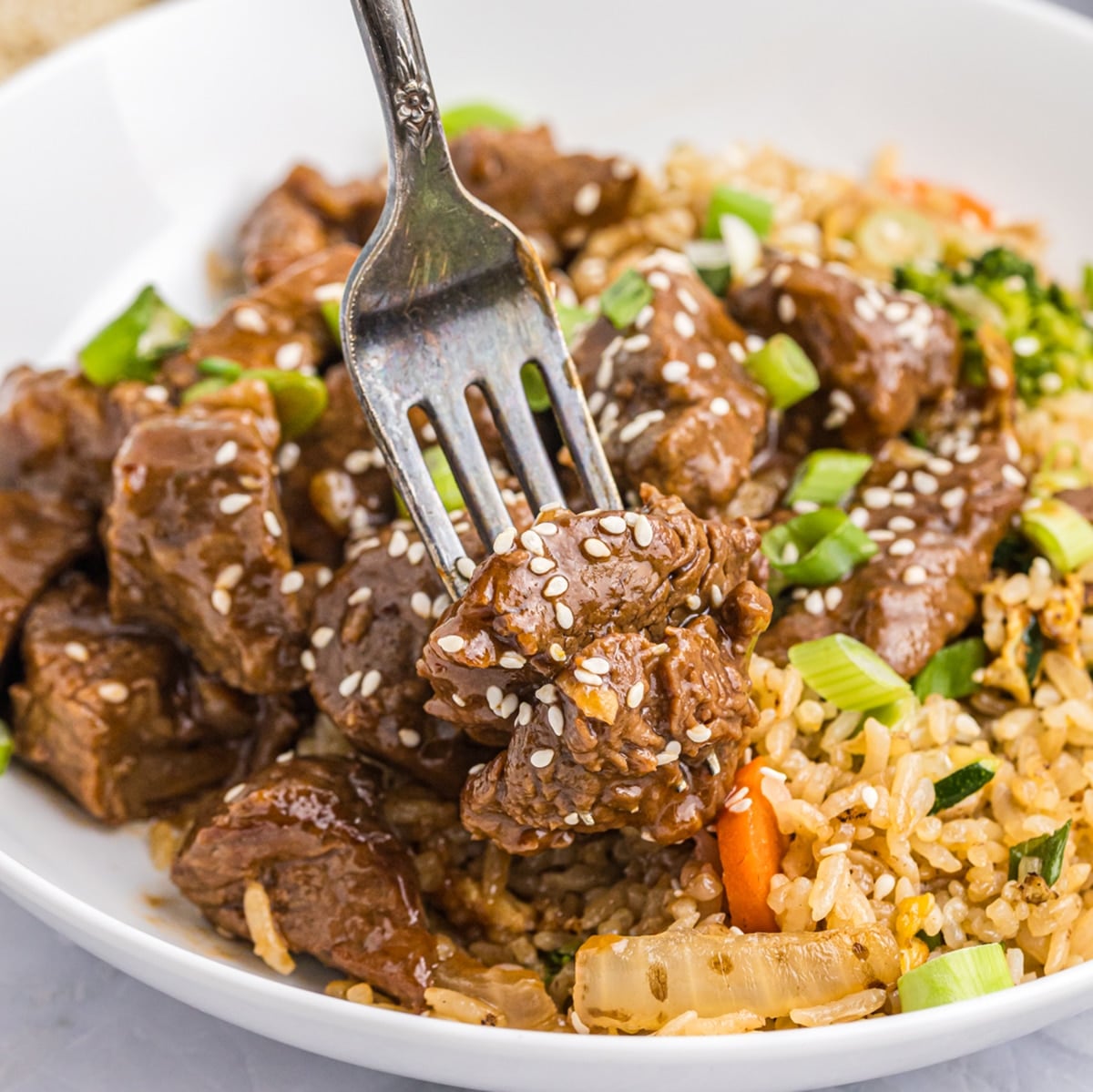 fork grabbing a bite of honey garlic steak bites on a plate with fried rice.