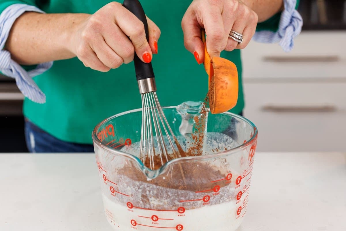 Adding cocoa powder to a large measuring cup with milk mixture.