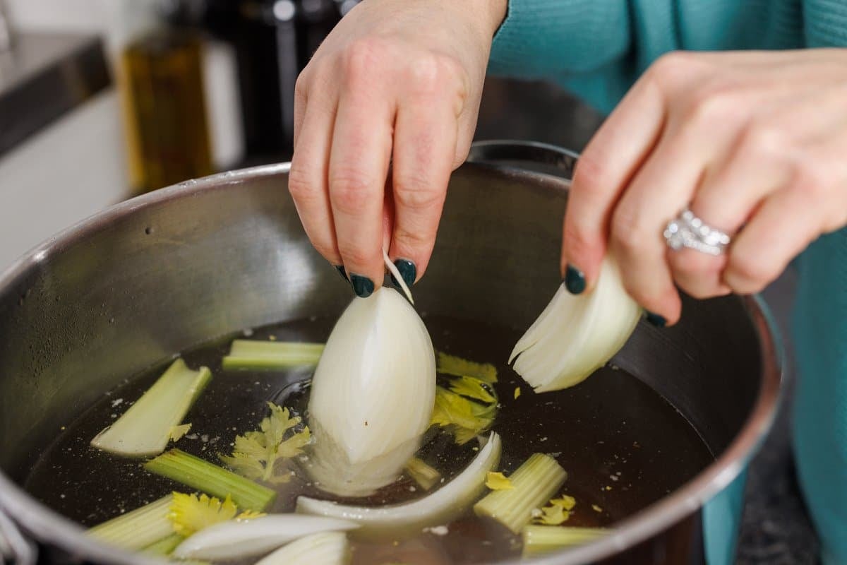Adding onion and celery to chicken stock.