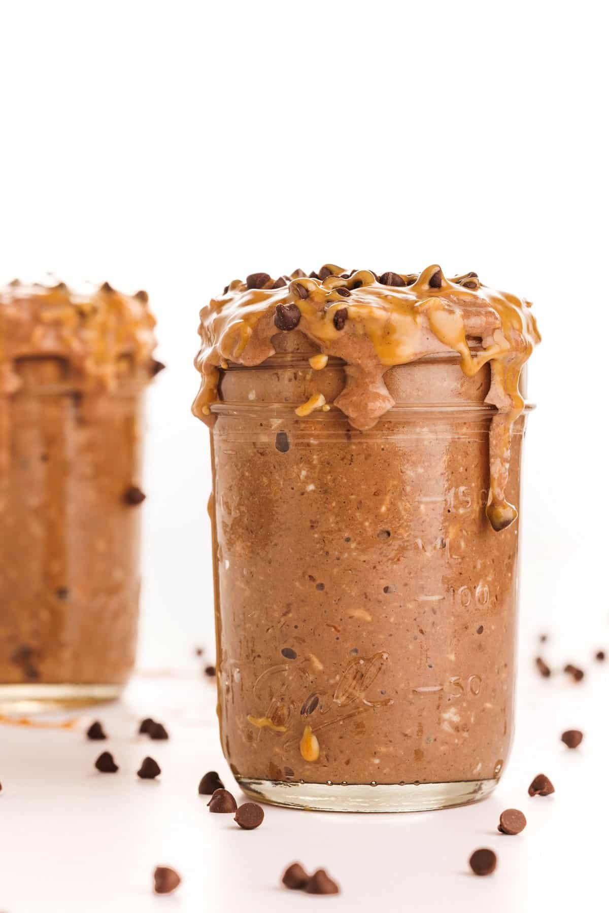 Chocolate peanut butter overnight oats in a mason jar topped with drizzled peanut butter and mini chocolate chips.