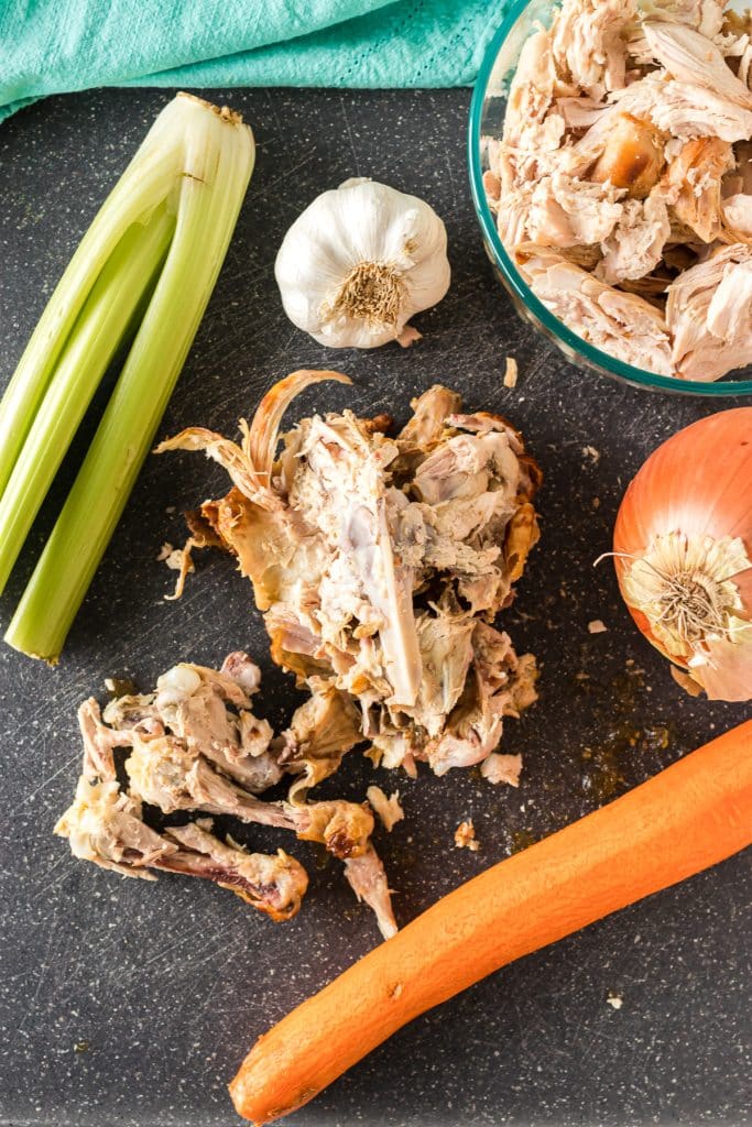 overhead shot of chicken bones and chopped veggies on a cutting board.