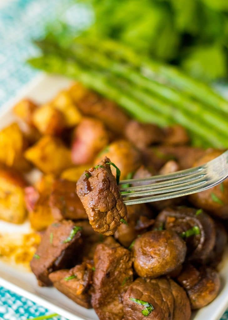 a steak bite on a fork in front of a plate of food.