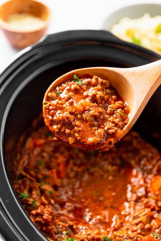 spoon lifting spaghetti sauce from a crockpot.