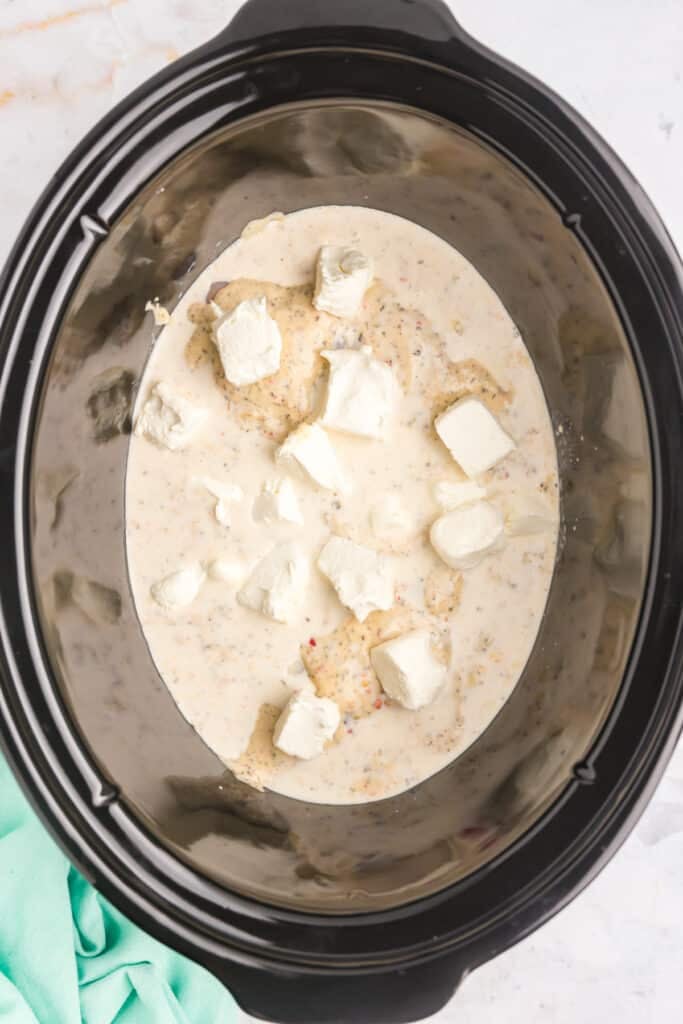 cubed cream cheese in a black crockpot.