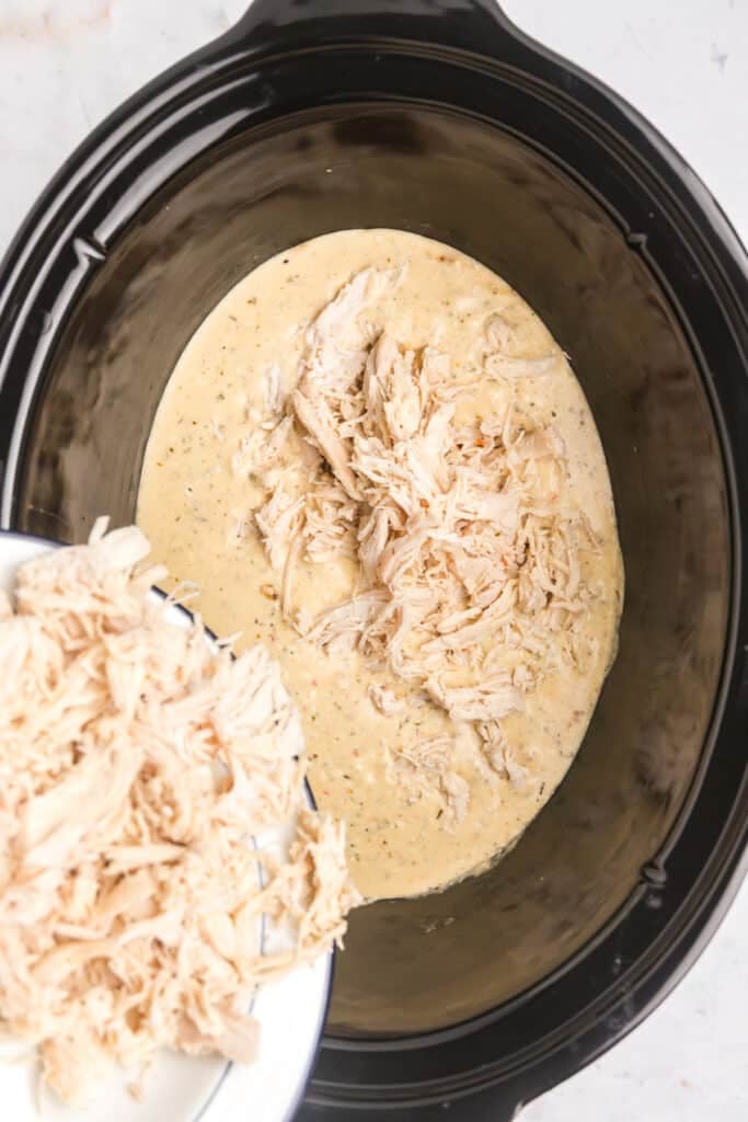 shredded chicken pouring into a crockpot with sauce.