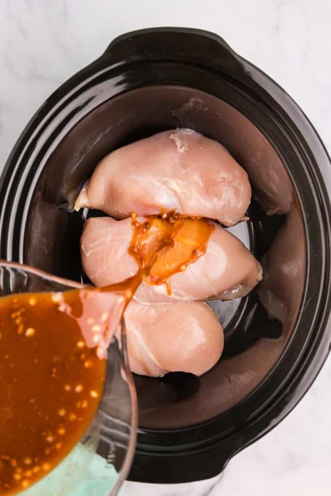honey lime marinade pouring over chicken breasts in a crockpot.