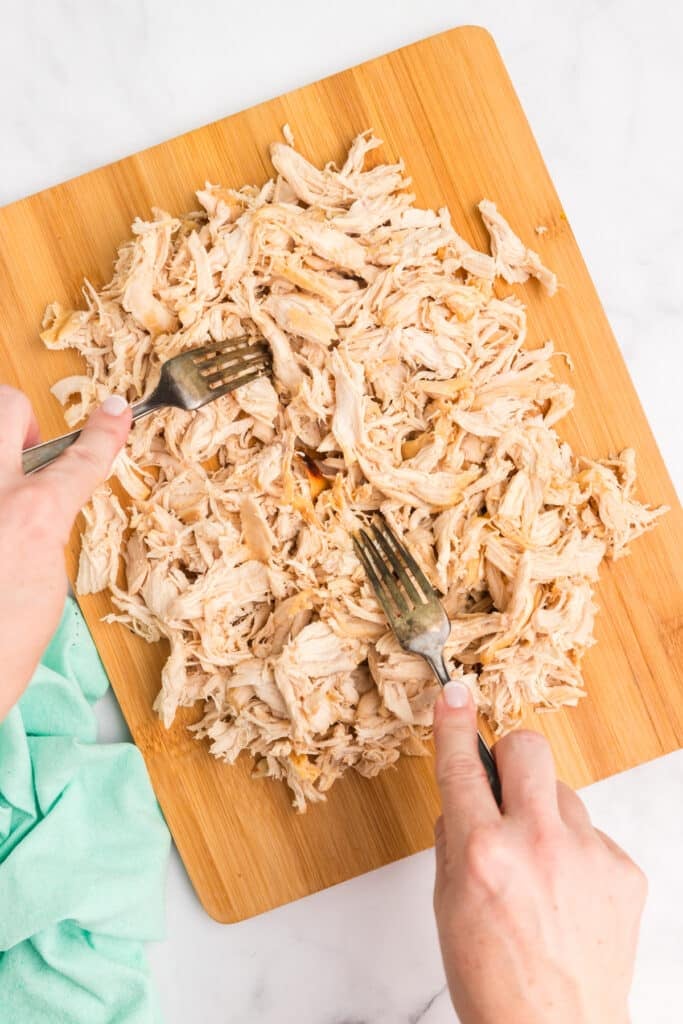 two forks shredding chicken on a cutting board.