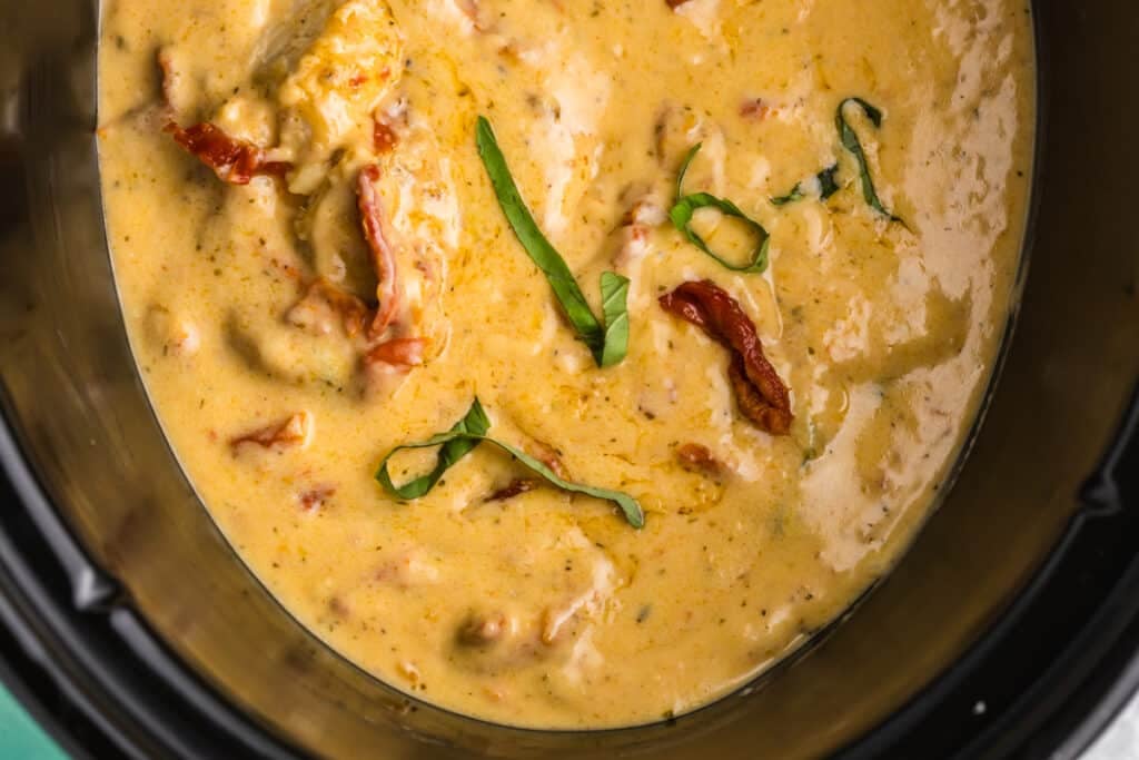 closeup of marry me chicken with sun dried tomatoes & basil in a crockpot.