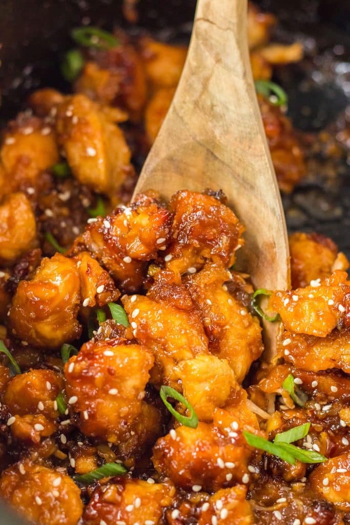 wooden spoon scooping orange chicken from a crockpot.