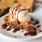 slice of chocolate chip cookie cake topped with ice cream and hot fudge.