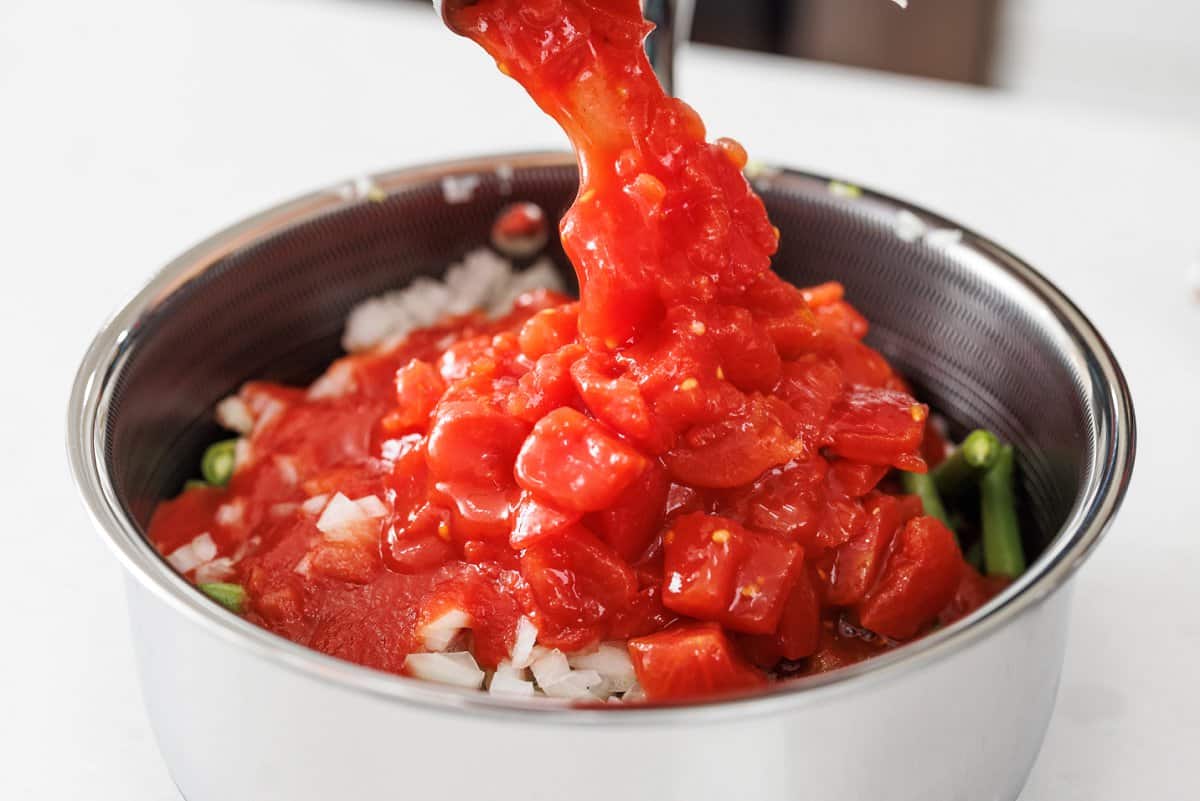 Pouring canned, diced tomatoes to pot with green beans.