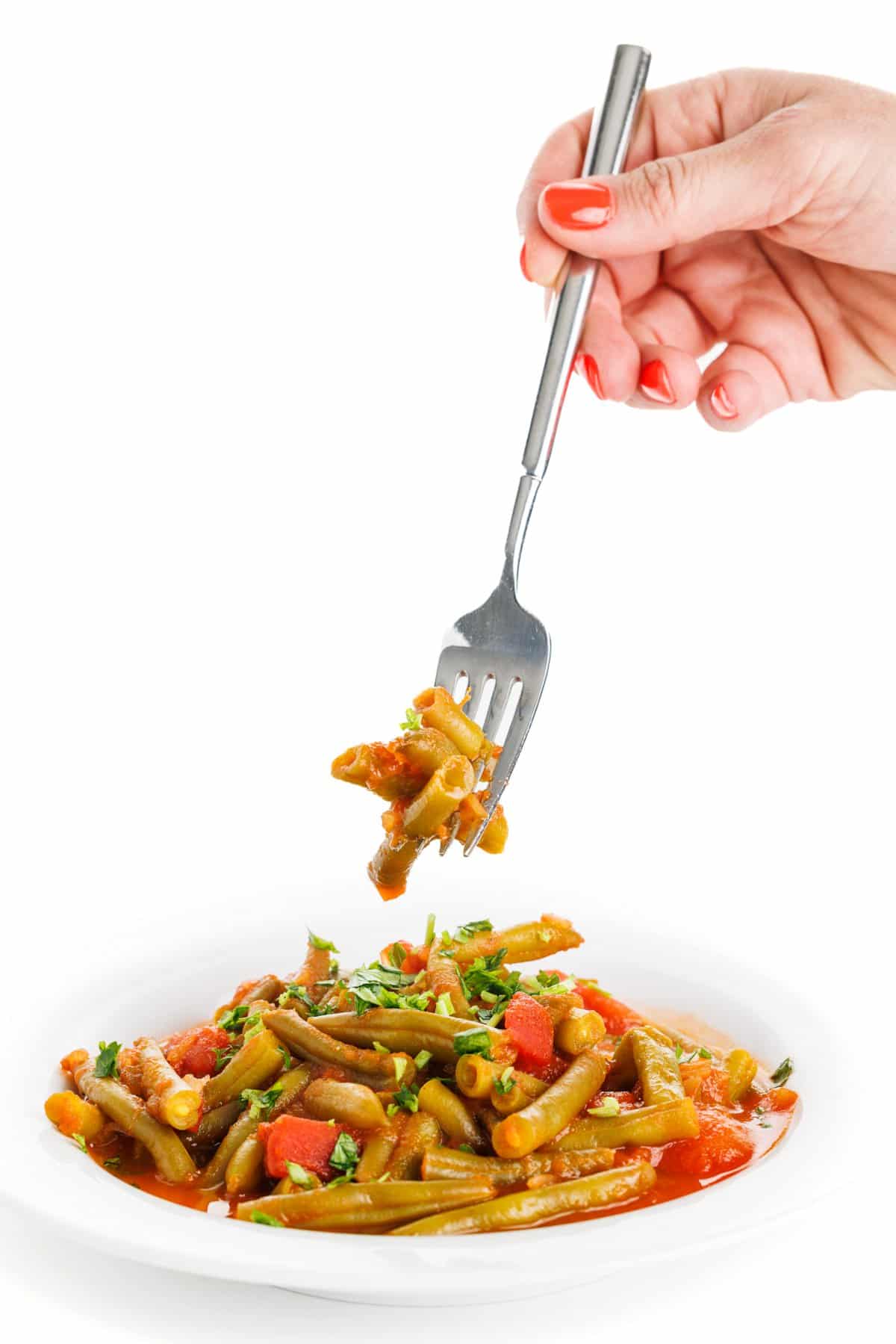 Forkful of stewed green beans over a plate.