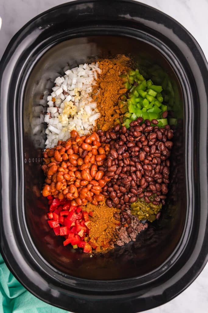 overhead shot of beans and diced veggies in a crockpot to make frito pie.