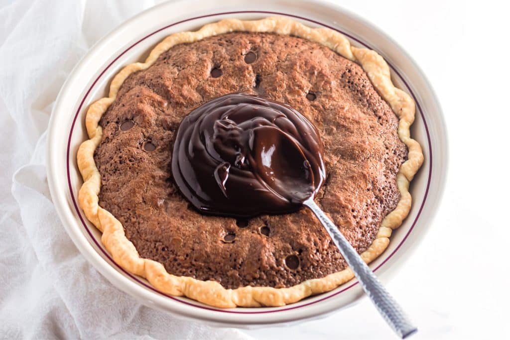 spoon spreading chocolate ganache on a brownie pie.